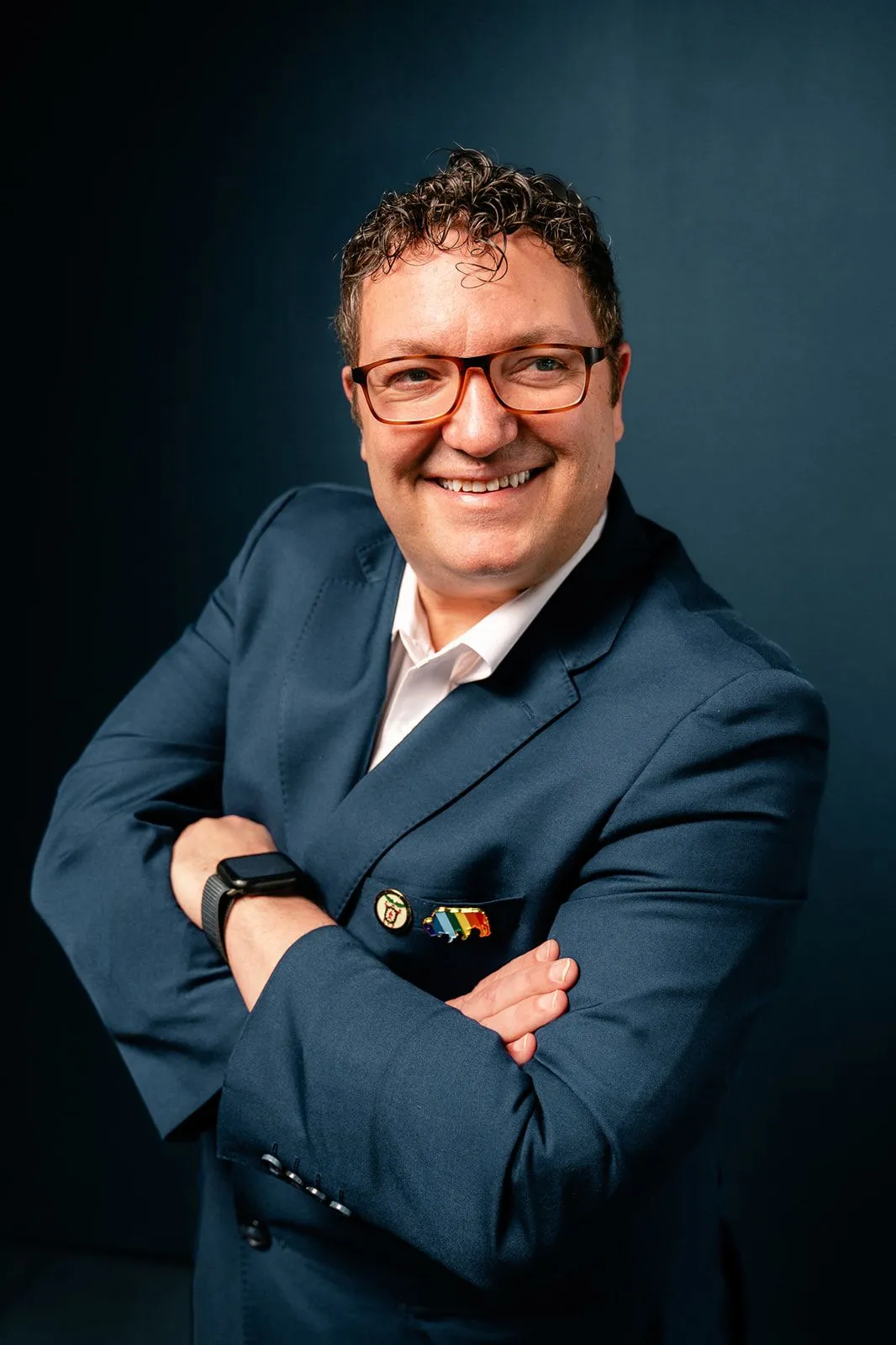 Billy Mawhiney smiling in a navy suit with his arms folded