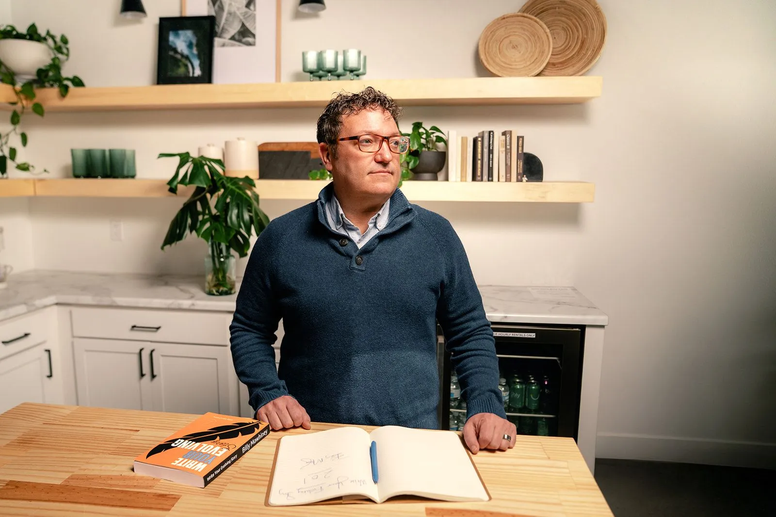 Billy Mawhiney standing at a kitchen table with an open notebook and his book