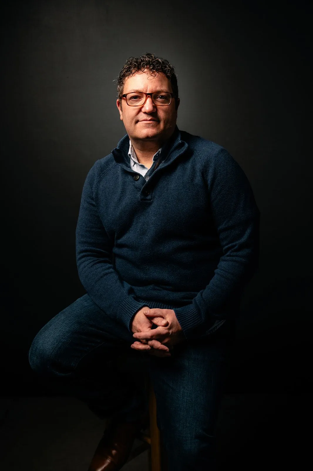 Billy Mawhiney seated on a stool in a dark studio portrait